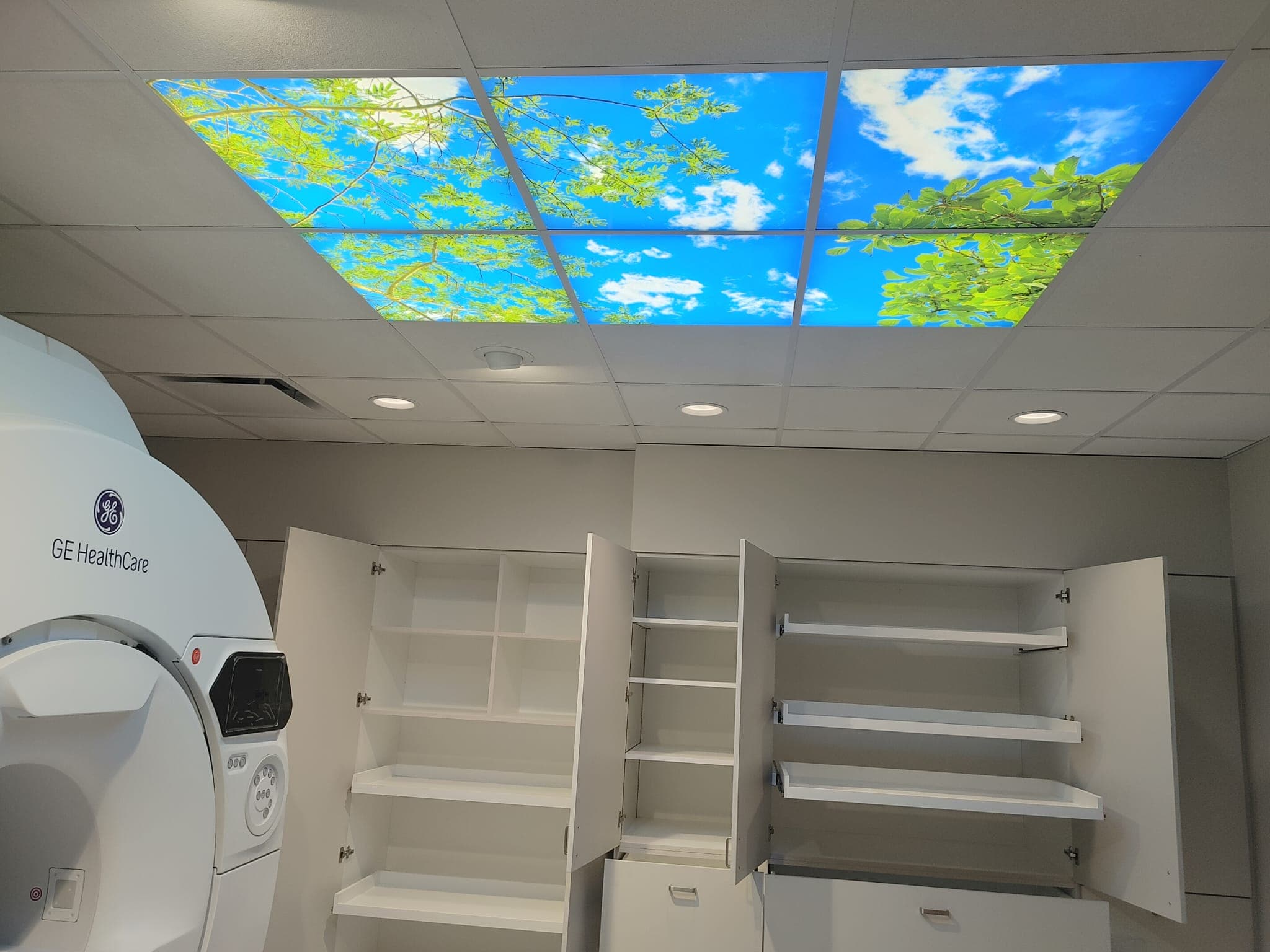 Completed MRI suite with a backlit sky-and-tree ceiling feature and built-in cabinetry
